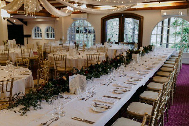 A long table in a room with tables and chairs set for a wedding reception.
