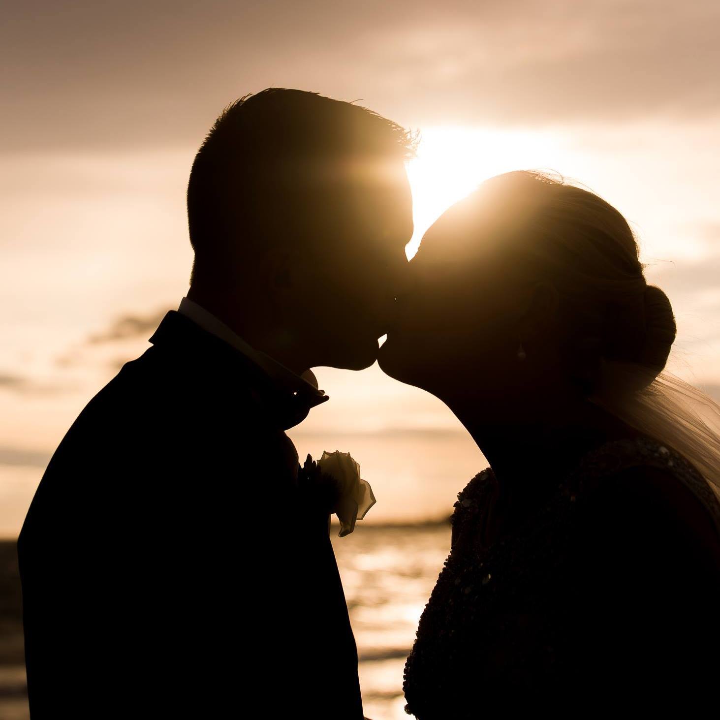 A silhouette of a bride and groom kissing at sunset