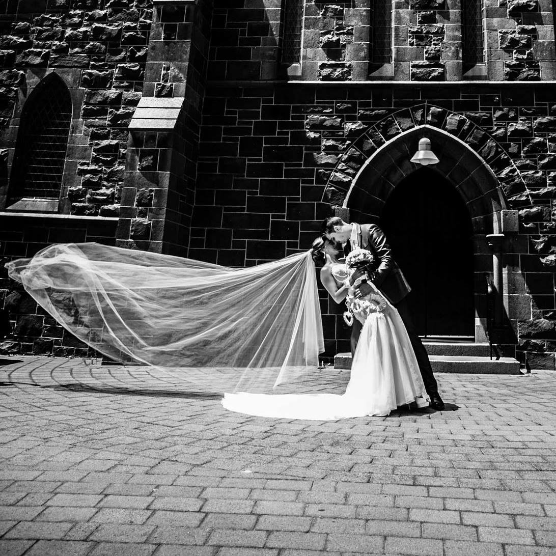 A black and white photo of a bride and groom kissing in front of a brick building