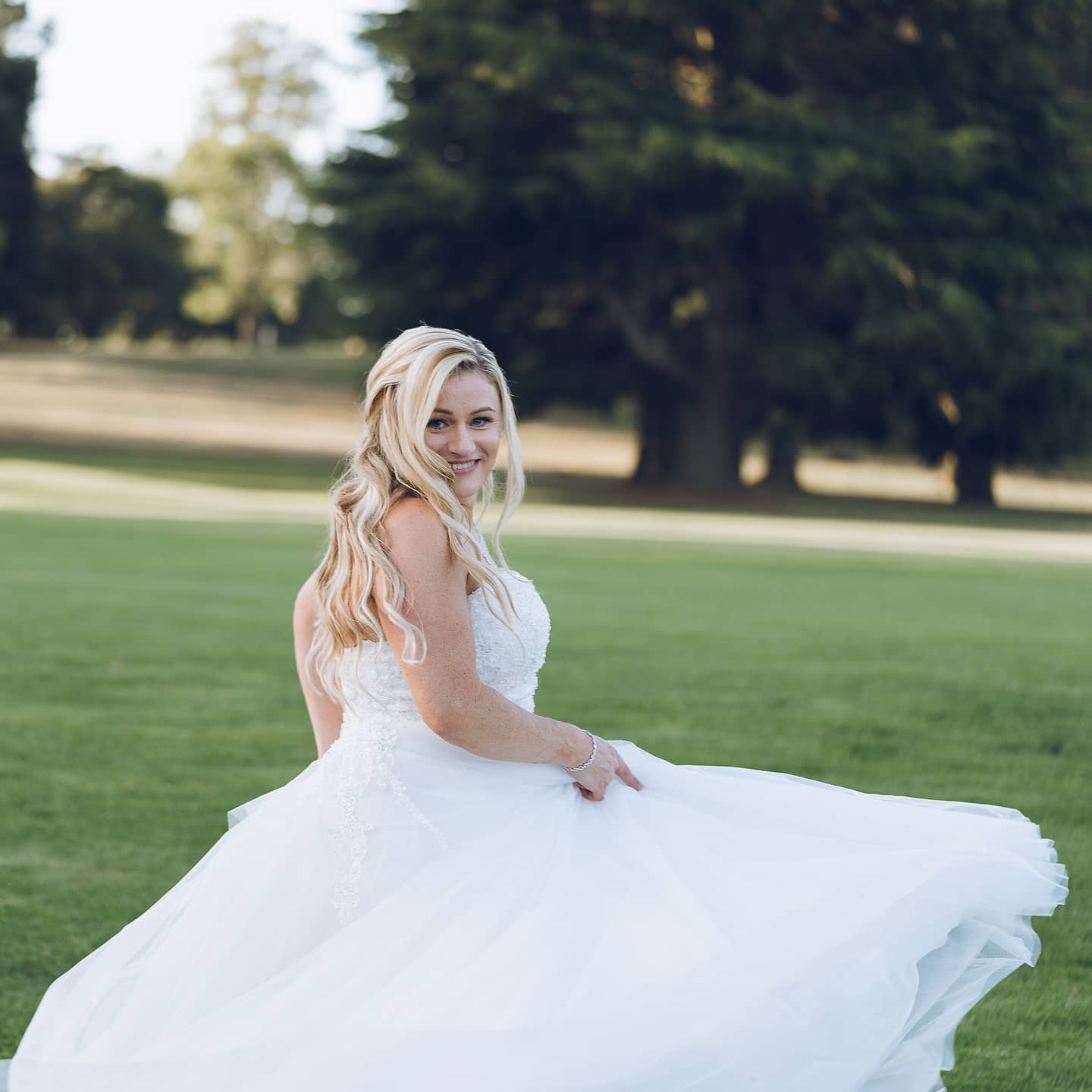A bride in a white wedding dress is sitting in the grass.