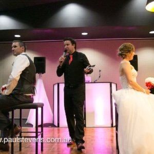 A man is holding a microphone in front of a bride and groom