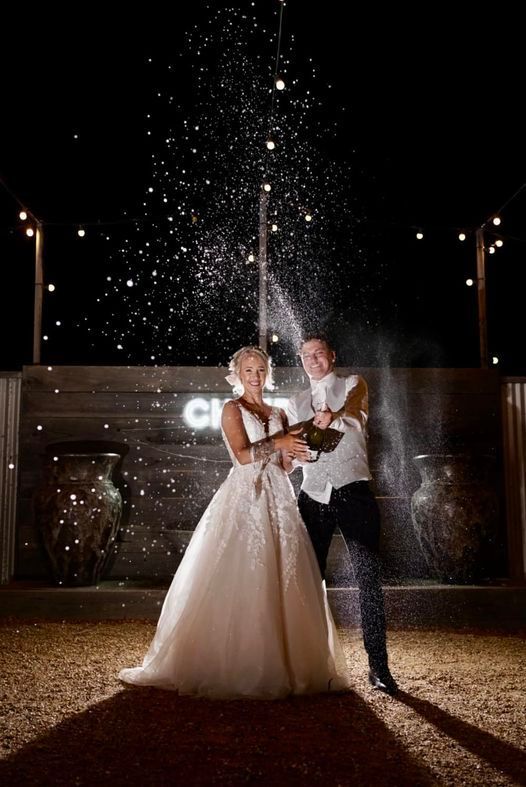A bride and groom are standing next to each other holding a bottle of champagne.