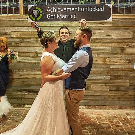 A bride and groom are standing in front of a sign that says achievement unlocked got married.