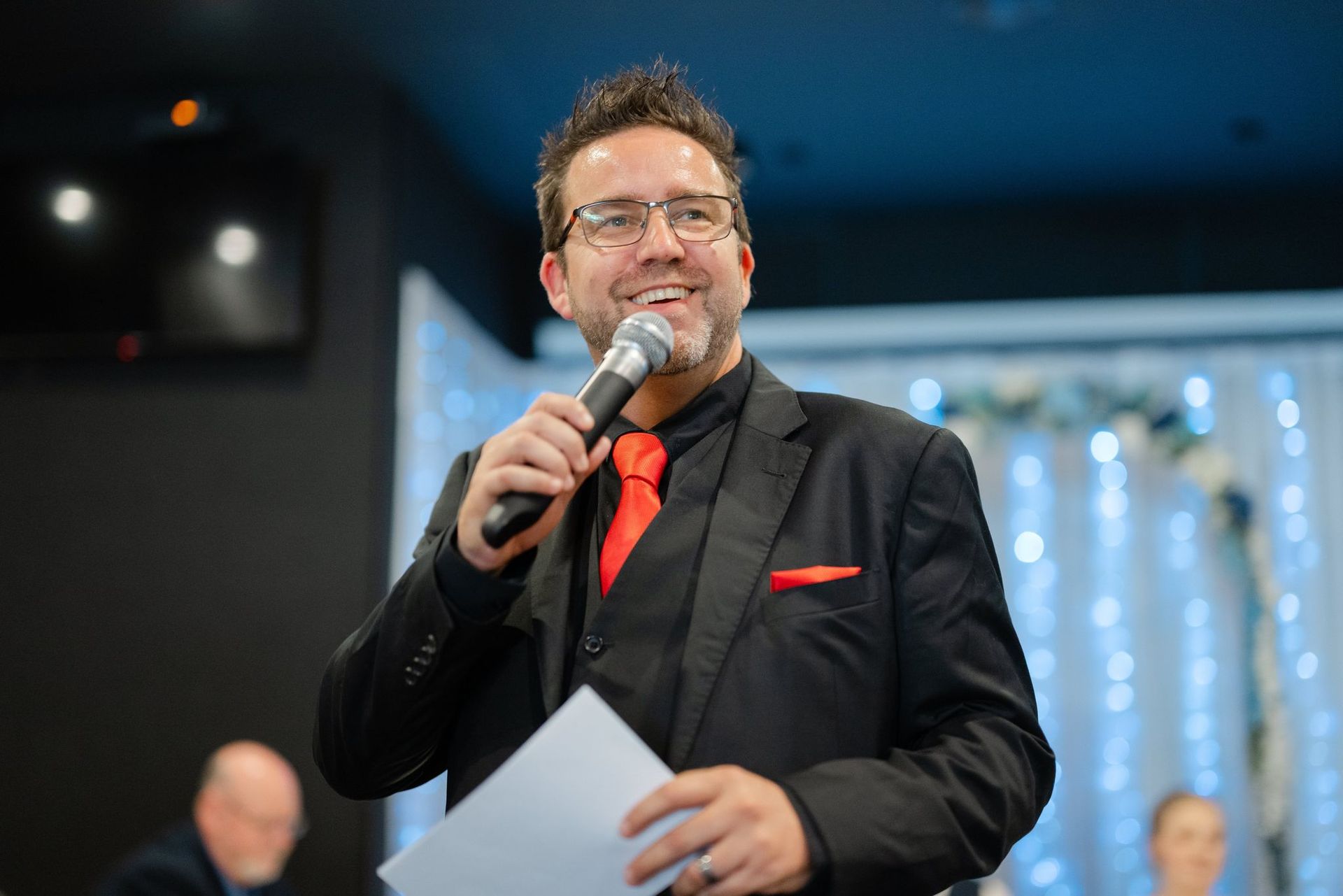 A man is holding a microphone in front of a bride and groom
