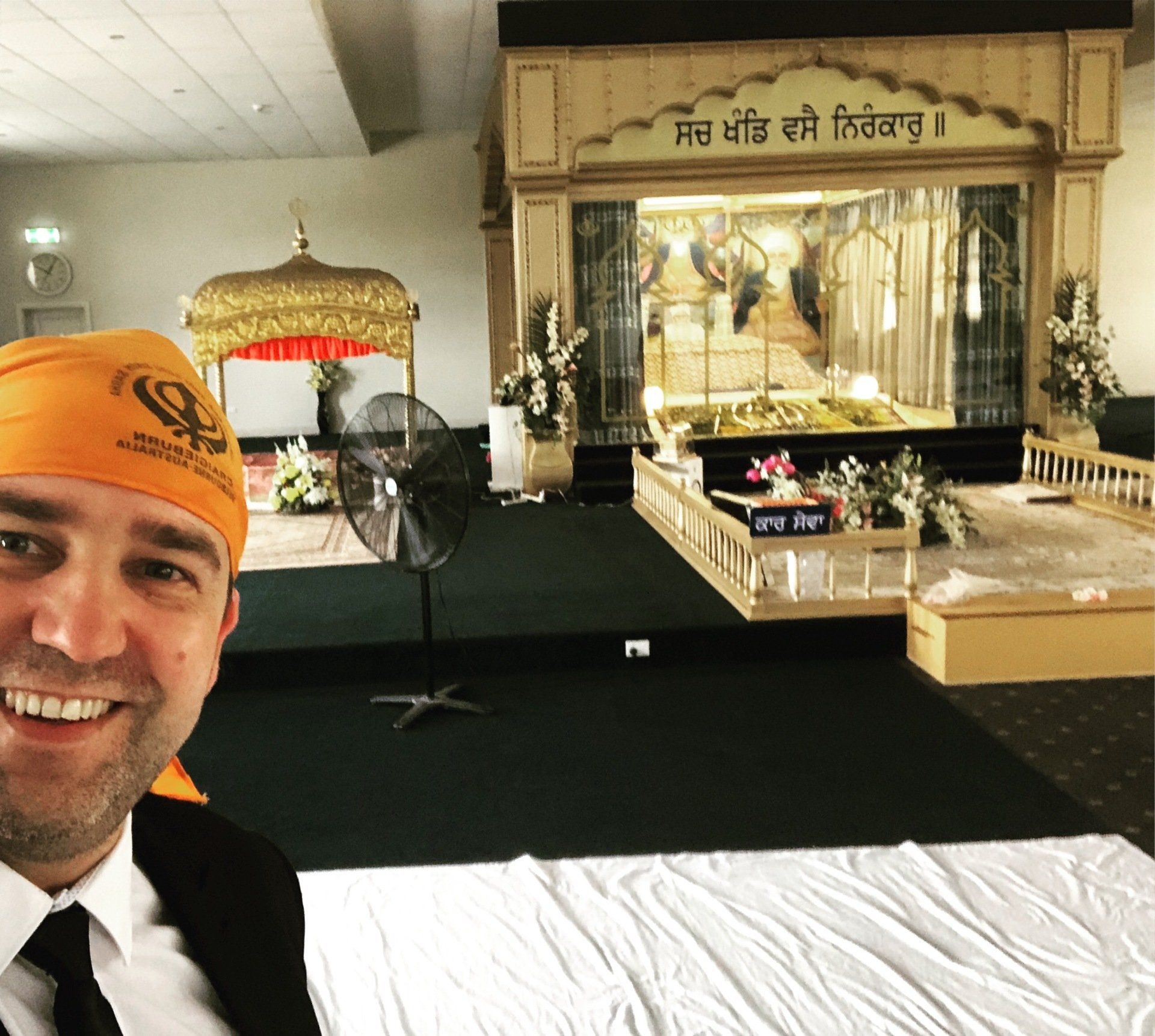 A man wearing an orange turban smiles in front of a temple