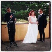A bride and groom are standing next to a man holding a microphone.
