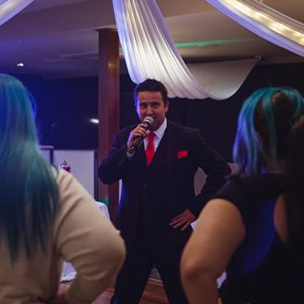 A man in a suit and tie is holding a microphone in front of a group of people.