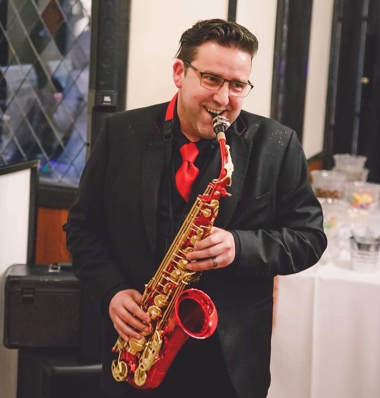 A man in a suit and tie is playing a red saxophone.