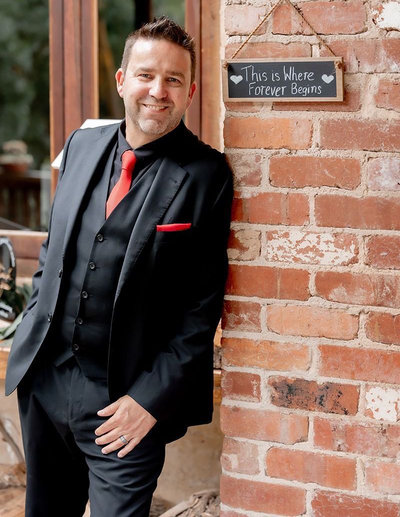 A man in a suit and tie is standing next to a brick wall.