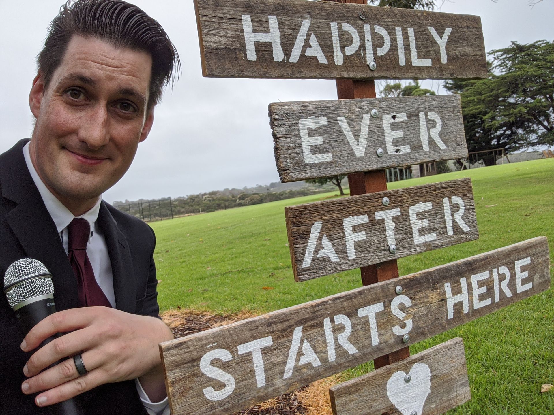 A man in a suit and tie is standing in front of a sign that says happily ever after starts here.
