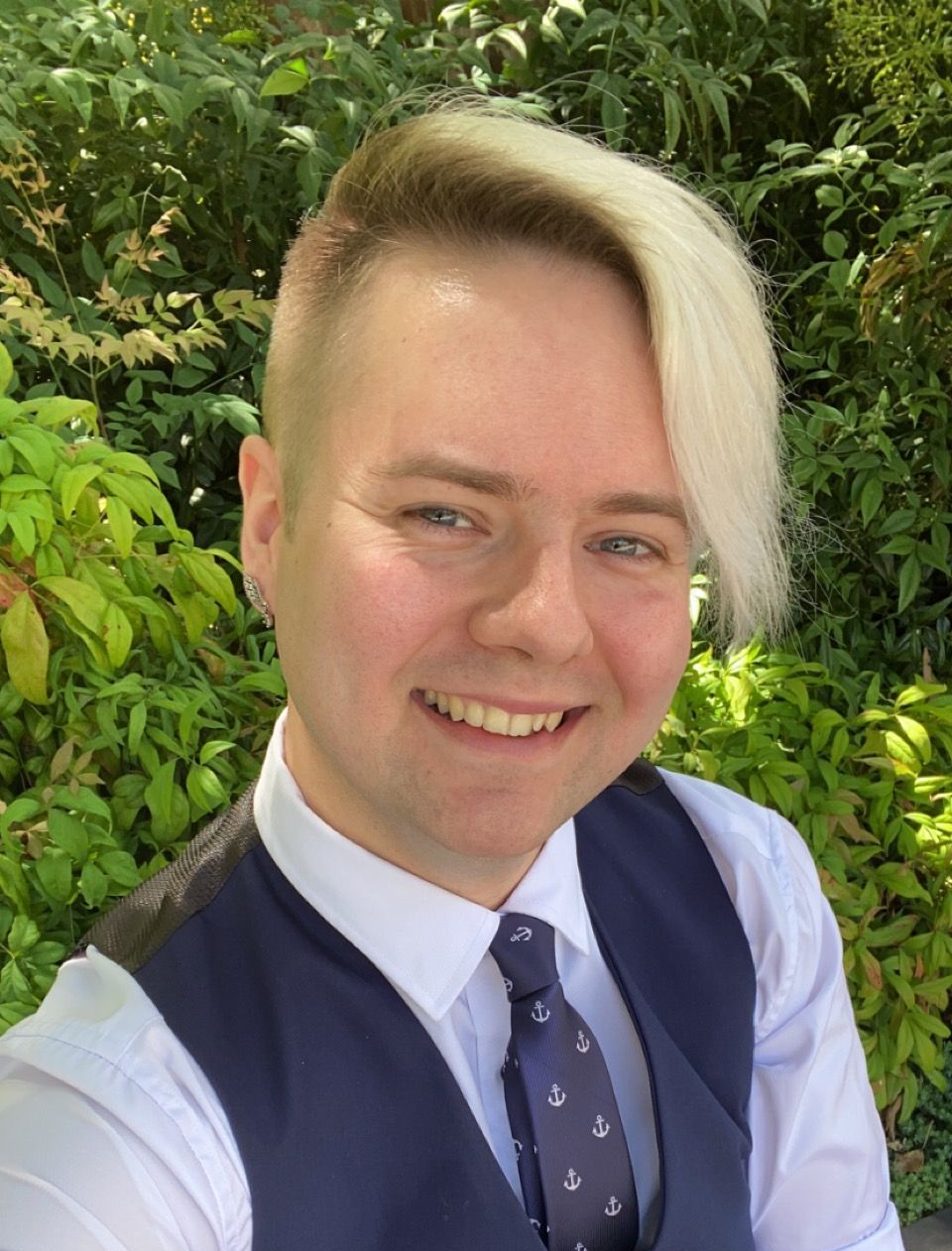 A man with blonde hair is wearing a white shirt and a blue vest and tie.