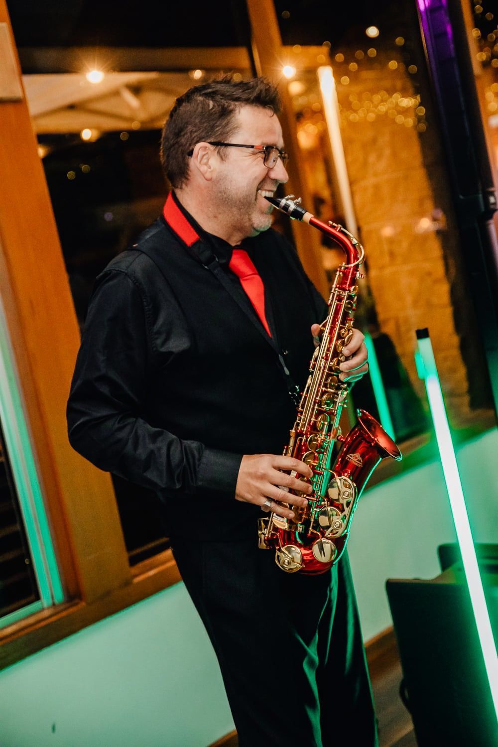 A man in a black shirt and red tie is playing a saxophone.