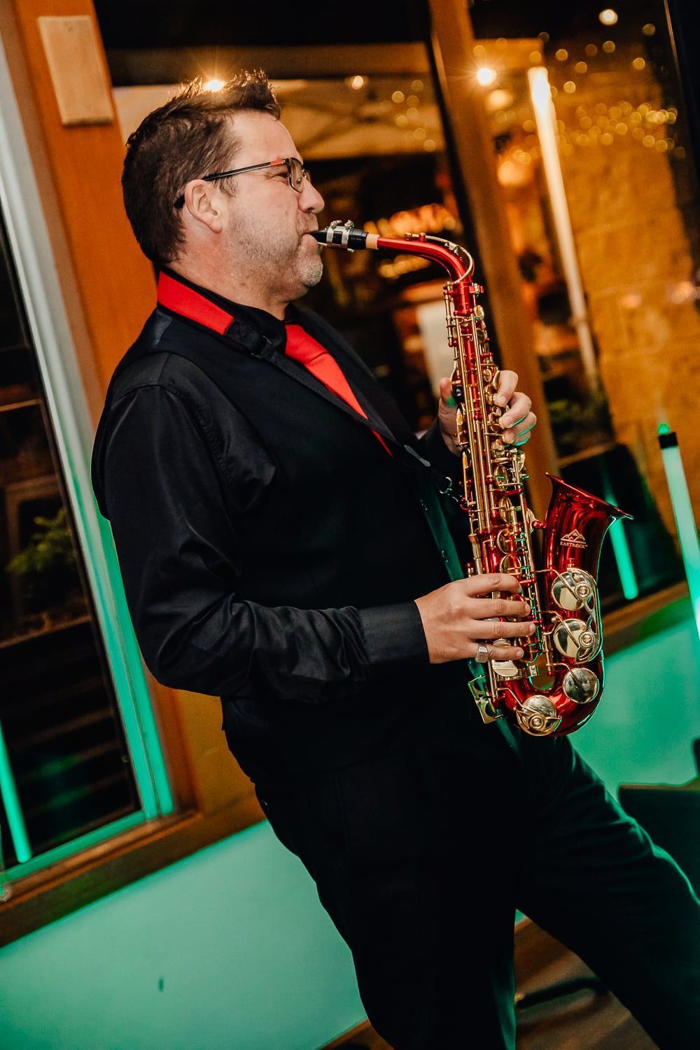 A man in a black shirt and red tie is playing a saxophone.