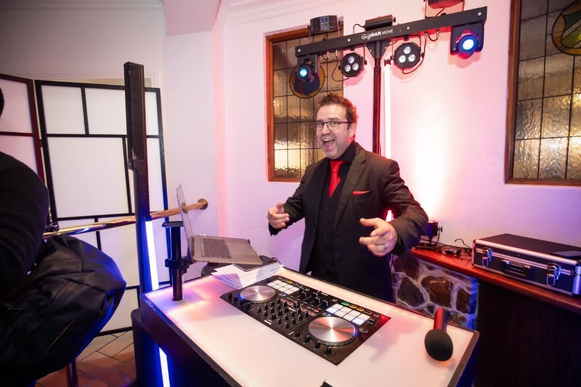 A man in a suit and red tie is standing in front of a dj booth.