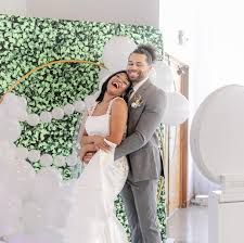 A bride and groom are posing for a picture in front of a flower wall.