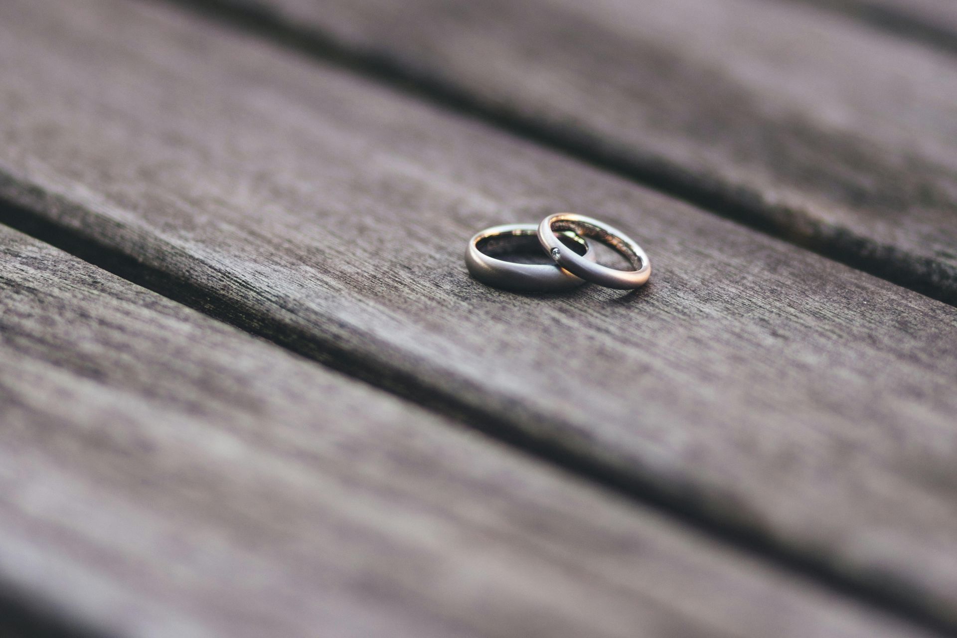 Two wedding rings on a weathered wooden surface, one silver and one gold.