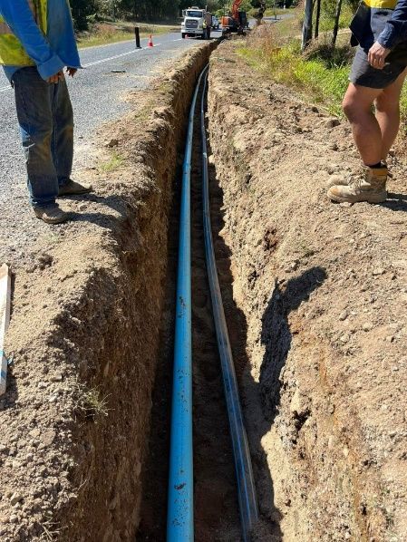 A Blue Pipe Is Being Installed In A Trench Next To A Road — Blue Dog Hire Qld In Midge Point, QLD