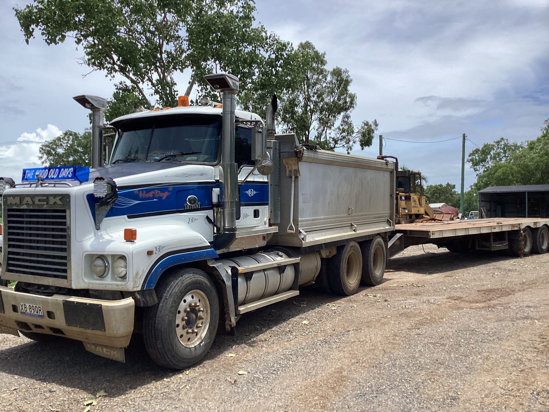 Mack truck with a flatbed trailer, parked on dirt. Blue and white cab, silver trailer — Blue Dog Hire Qld In Midge Point, QLD
