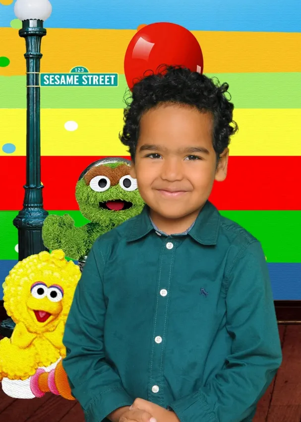 Boy smiles in front of Sesame Street characters, colorful backdrop, and a street sign.