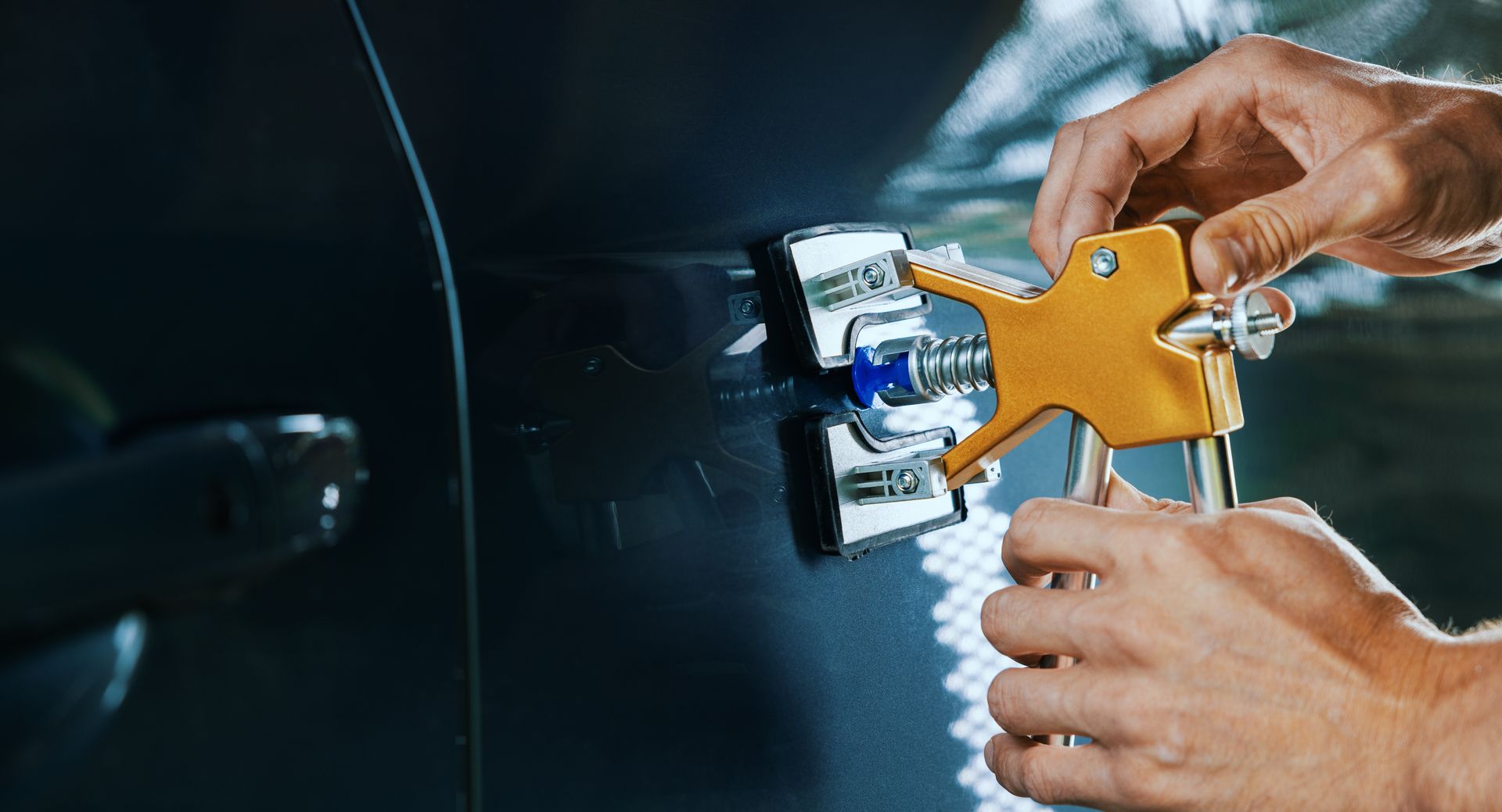 Hands using a dent puller to repair a dark car's body.
