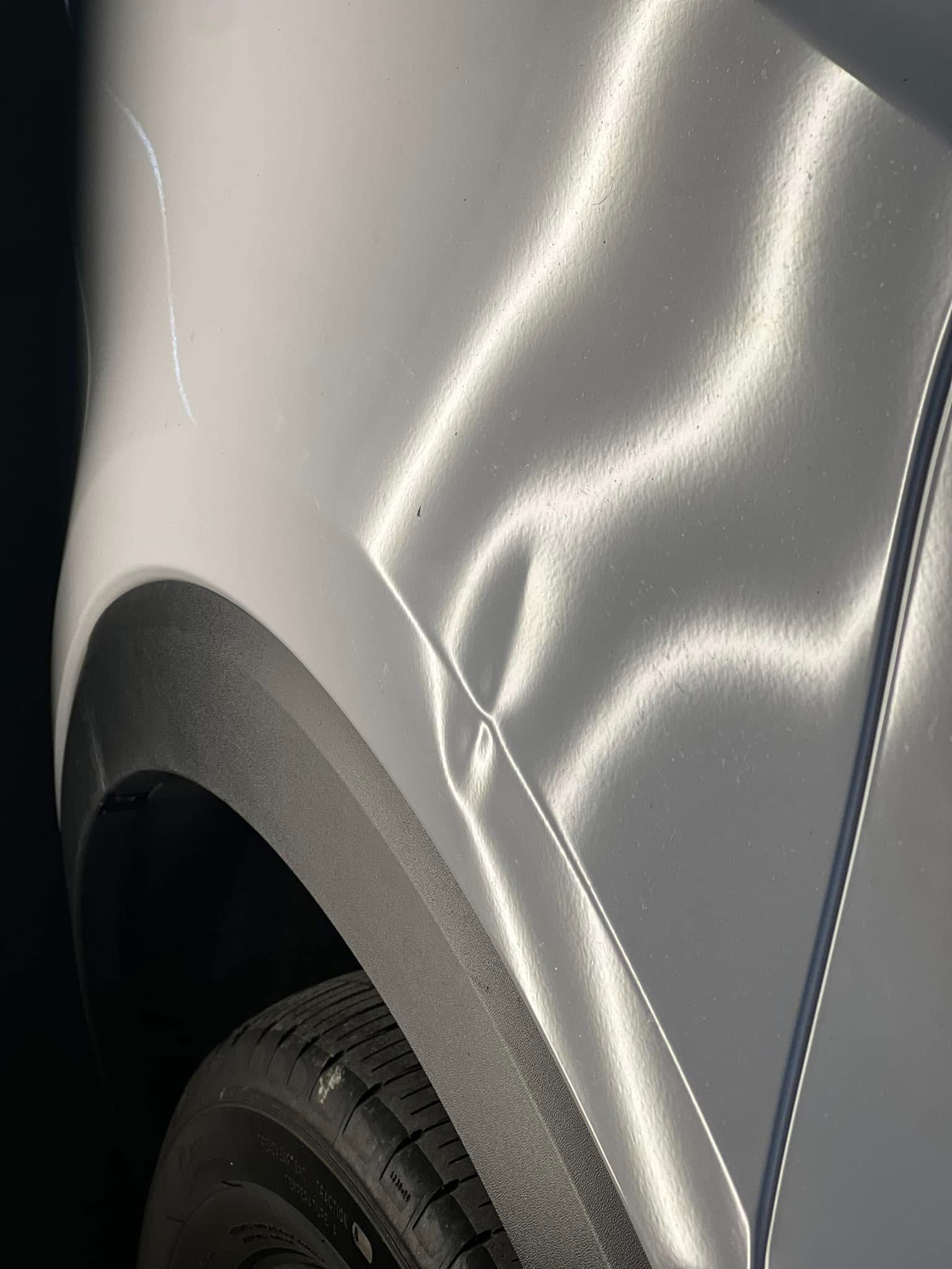 A dented silver car fender with a vertical crease near the black plastic wheel well trim.