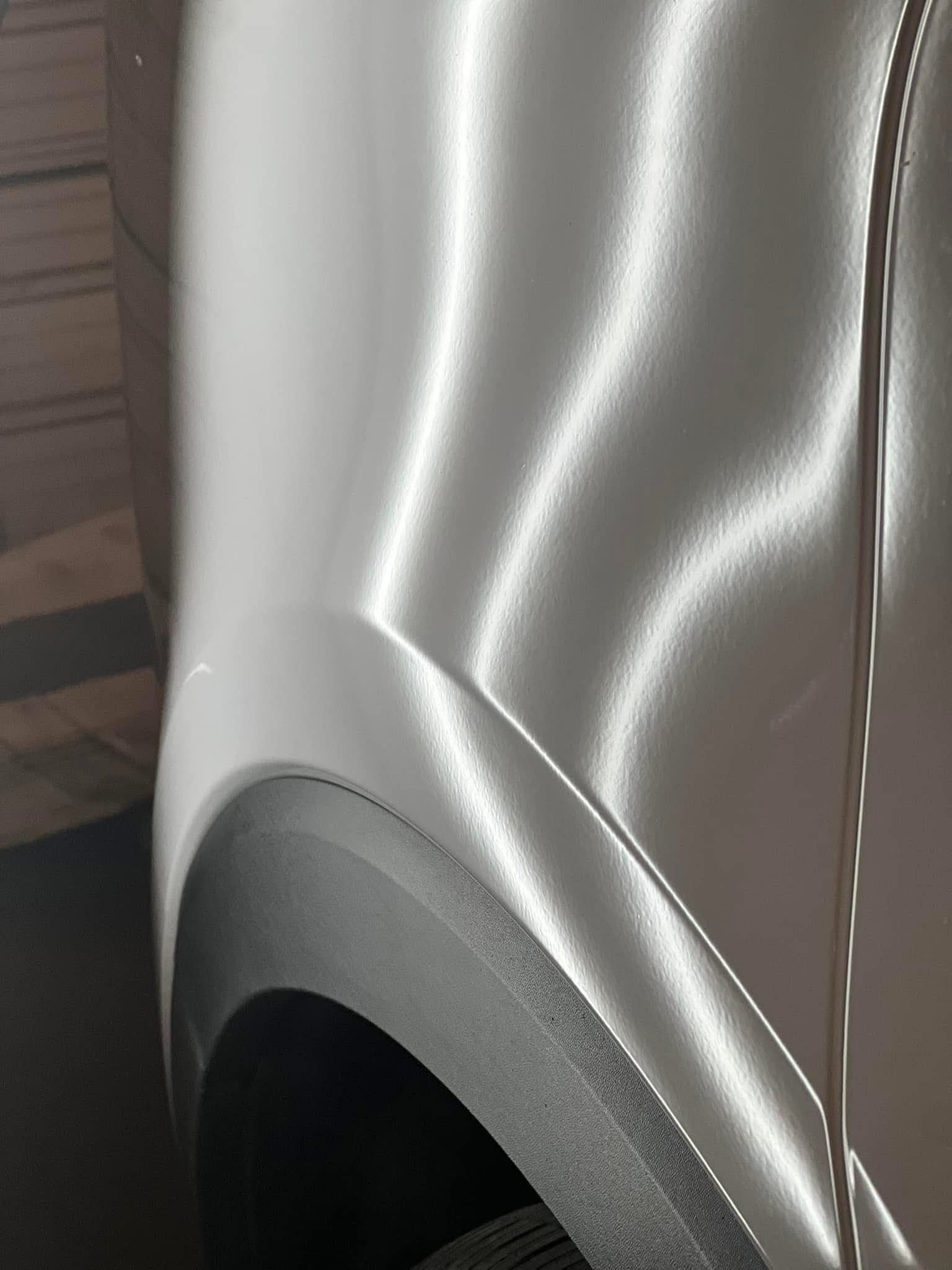 Close-up of a silver car fender above a black tire well, showing body lines and a smooth, metallic finish.