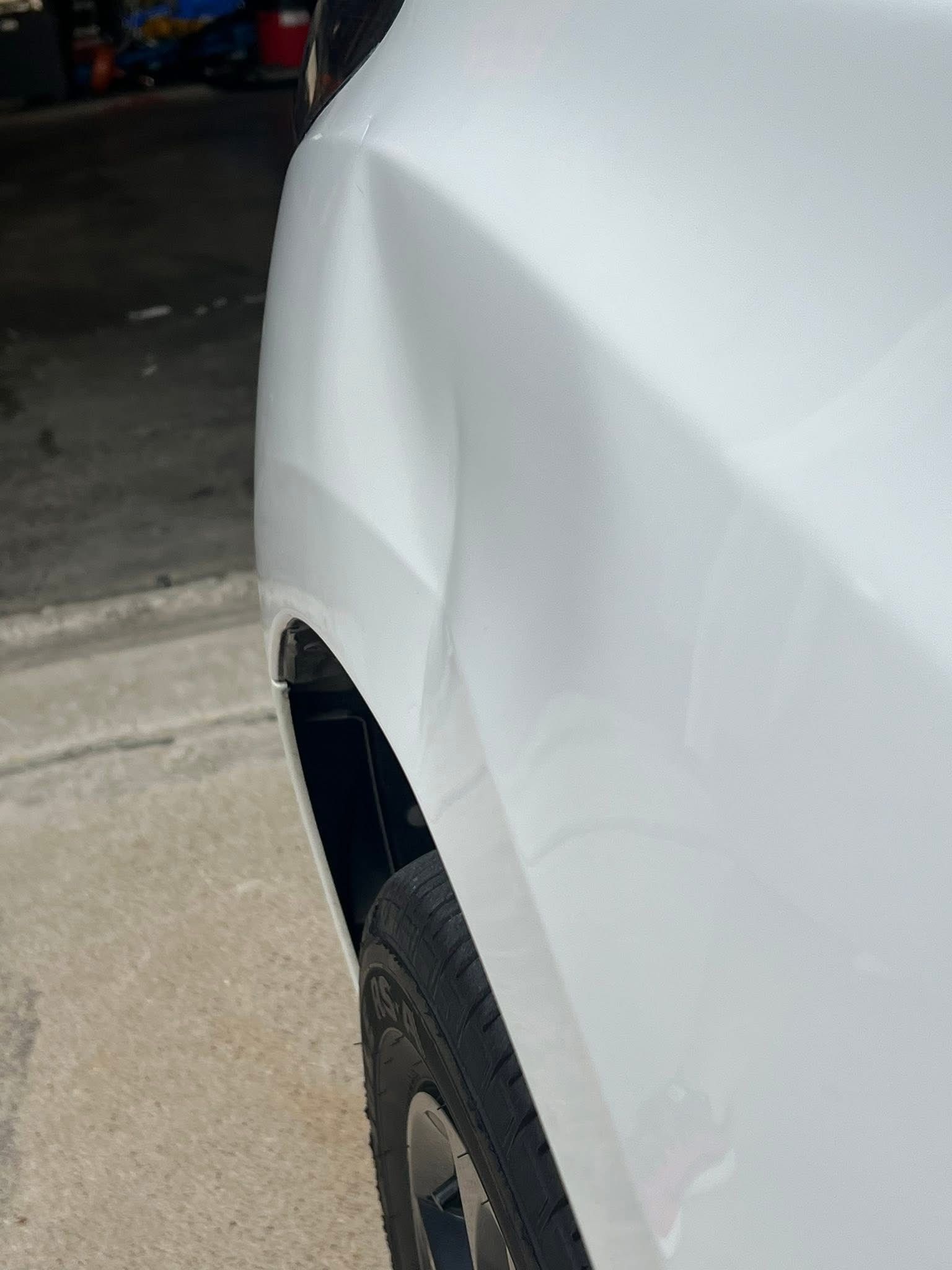 A close-up view of a large, shallow dent on the white rear quarter panel of a vehicle above the wheel well.