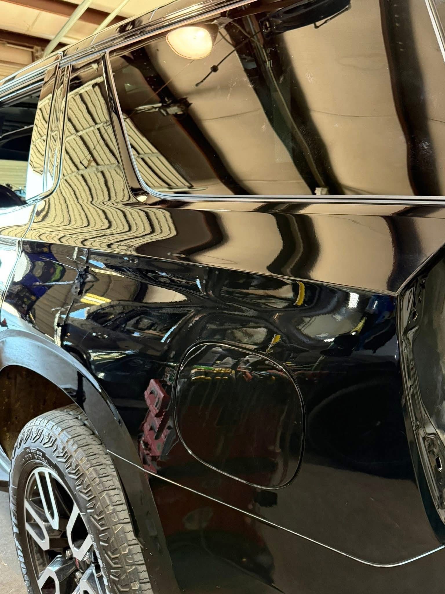 A close-up view of the side of a shiny black pickup truck, highlighting the fuel door and a large tire.