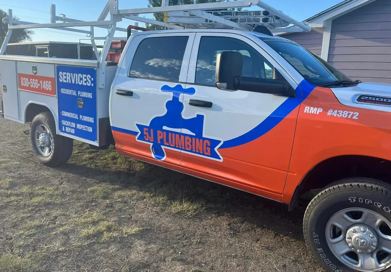 Red-and-blue plumbing service pickup truck parked on grass beside a house