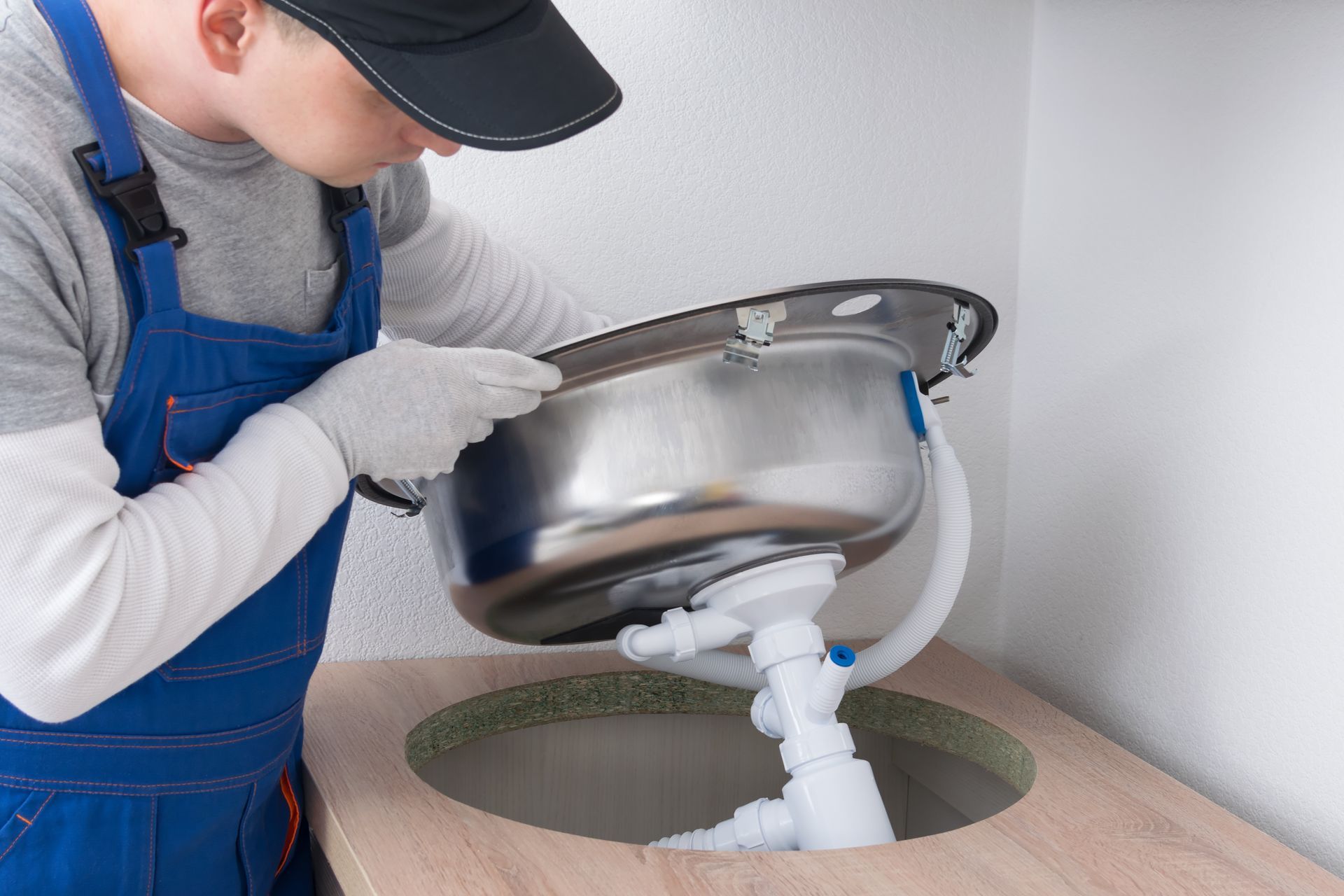 A person in blue work overalls installing a stainless steel kitchen sink into a countertop.