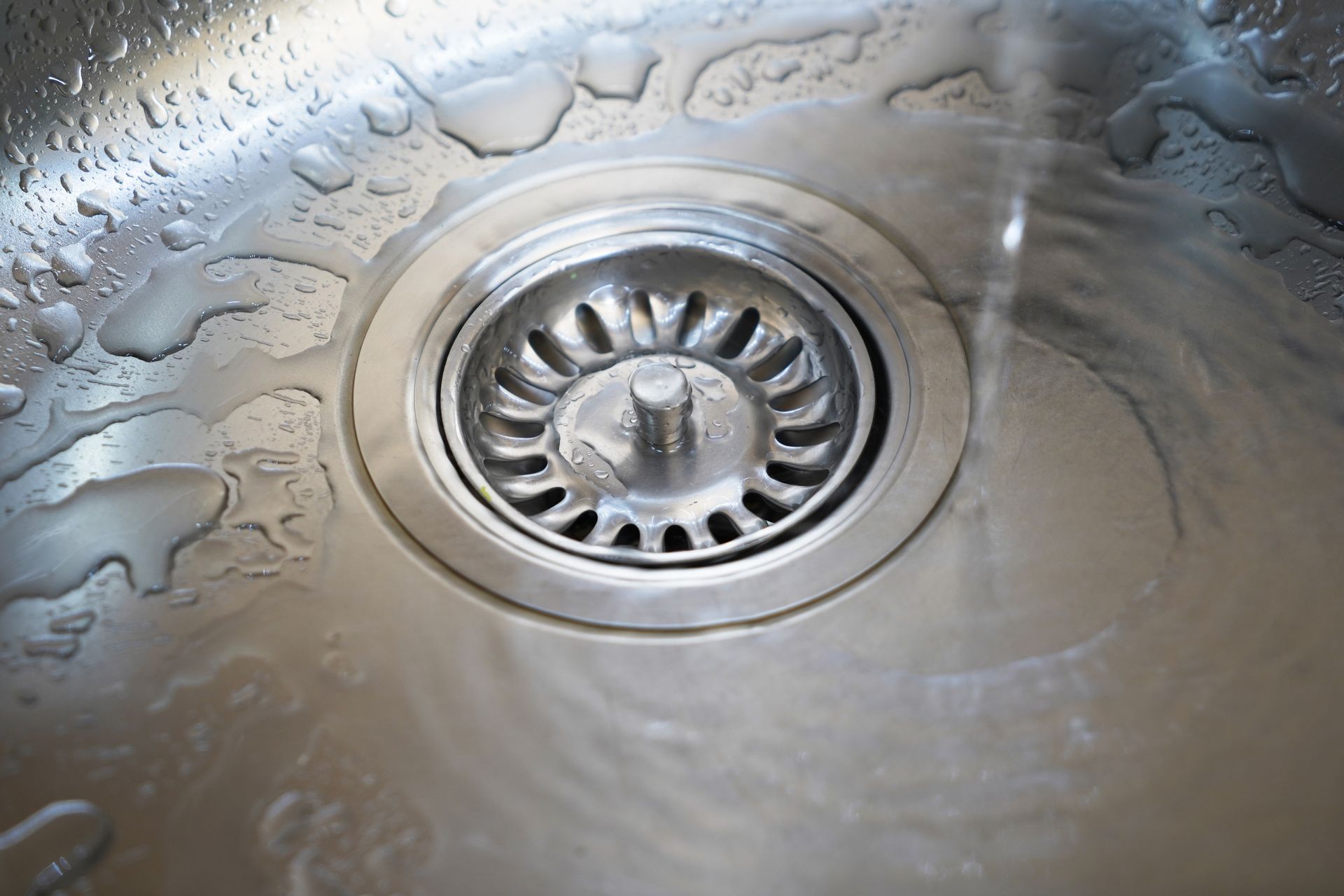 A close-up view of a metal kitchen sink drain with water running into it.