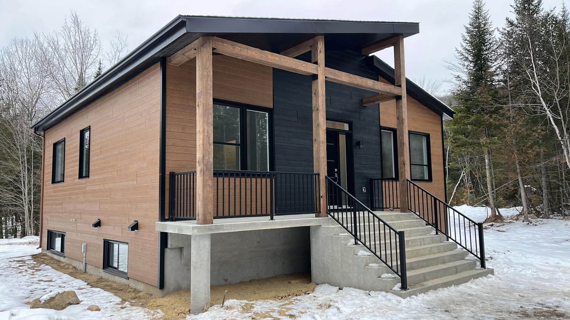 Maison moderne en briques avec porche couvert et escaliers dans un paysage enneigé.