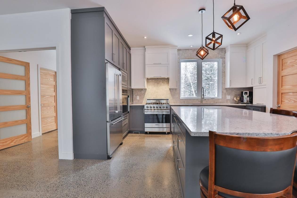 Cuisine moderne avec armoires grises et blanches, électroménagers en acier inoxydable et un grand îlot.