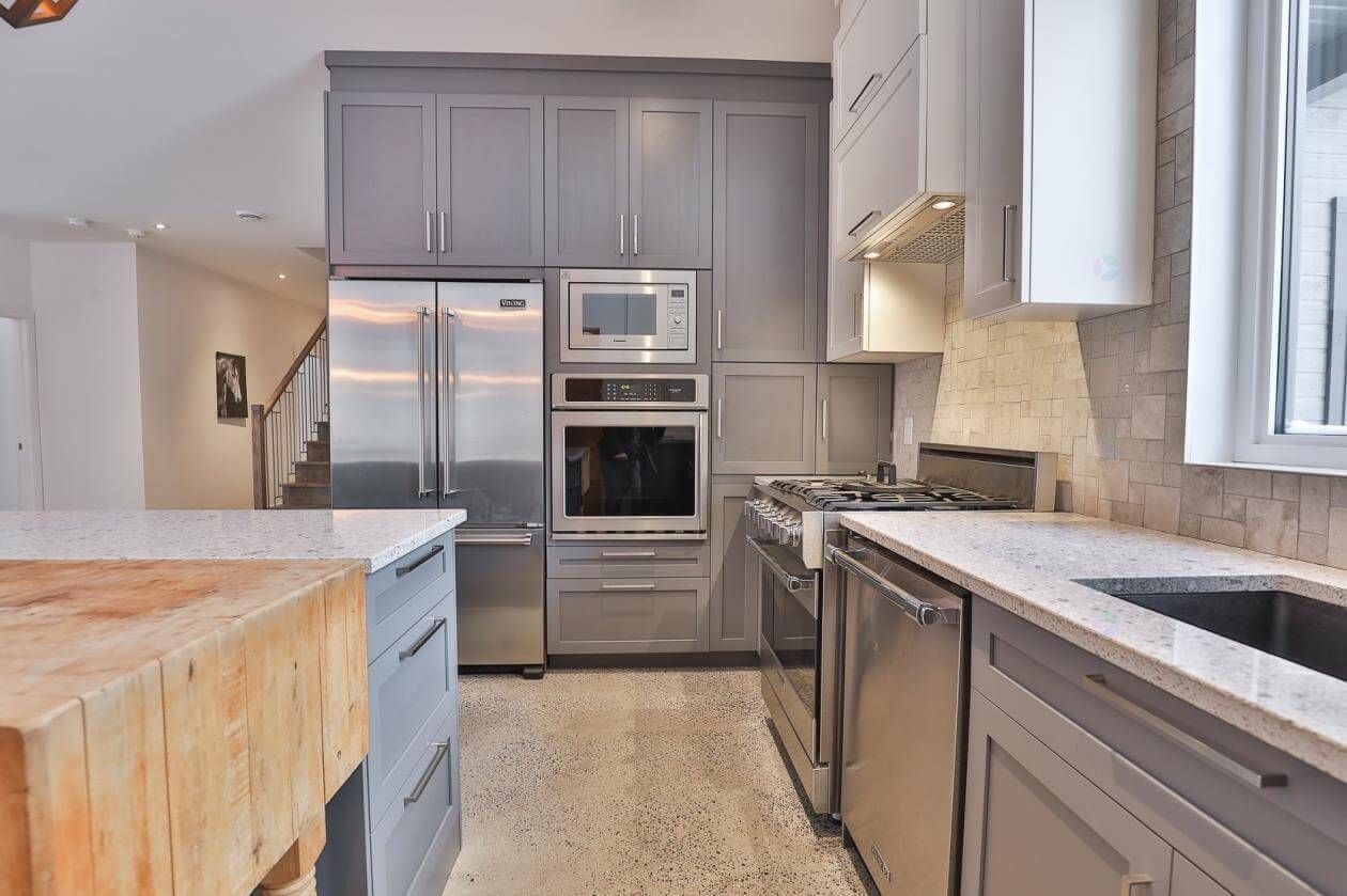 Cuisine avec armoires grises, électroménagers en acier inoxydable et îlot central en bois massif.