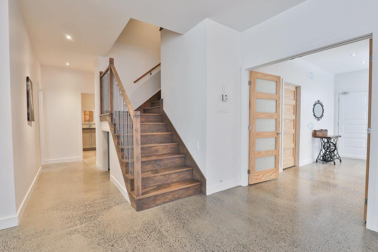 Entrée avec escalier et parquet clair, menant au deuxième étage. Murs blancs et portes en bois.