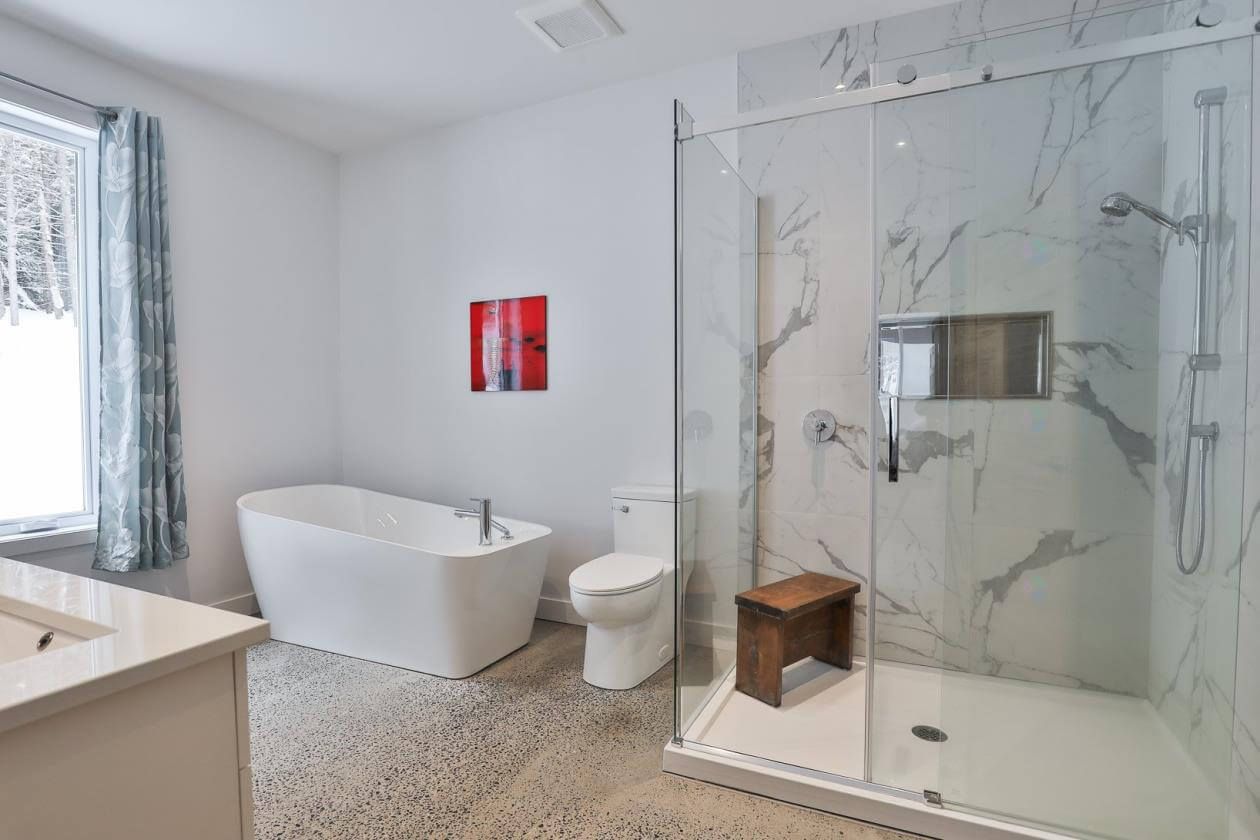 Salle de bains moderne avec baignoire îlot, douche en verre et mur d'accent en marbre.