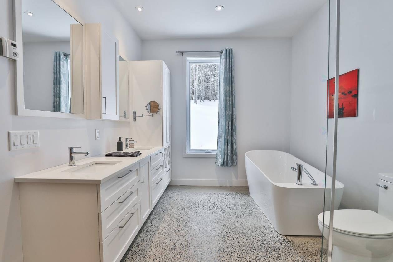 Salle de bains moderne blanche avec baignoire îlot, grande vasque et fenêtre avec rideau à motifs.