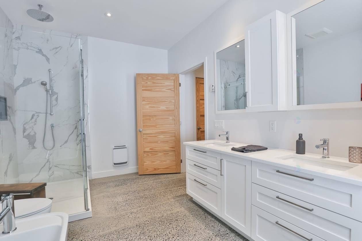 Salle de bains moderne avec meubles blancs, douche en marbre et porte en bois.
