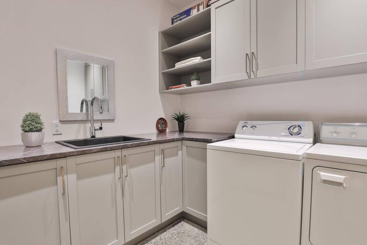 Buanderie avec placards, appareils électroménagers et évier blancs ; tons neutres.