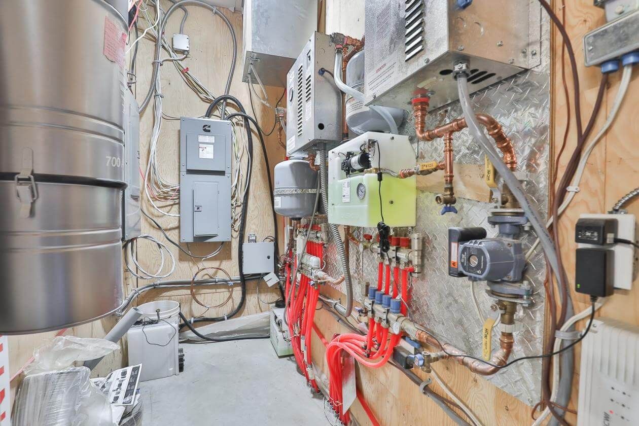 Systèmes électriques et de plomberie installés sur un mur en bois, comprenant des tuyaux, des boîtes et un grand réservoir métallique.