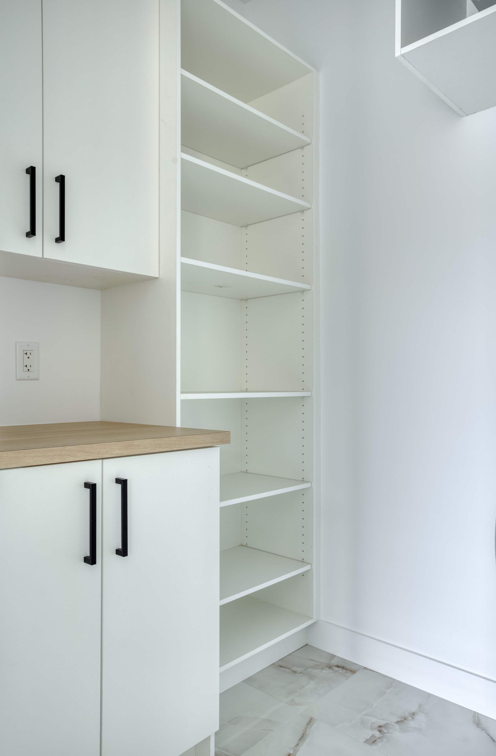 Étagères et placards intégrés blancs avec poignées noires, un plan de travail en bois clair et un sol carrelé.