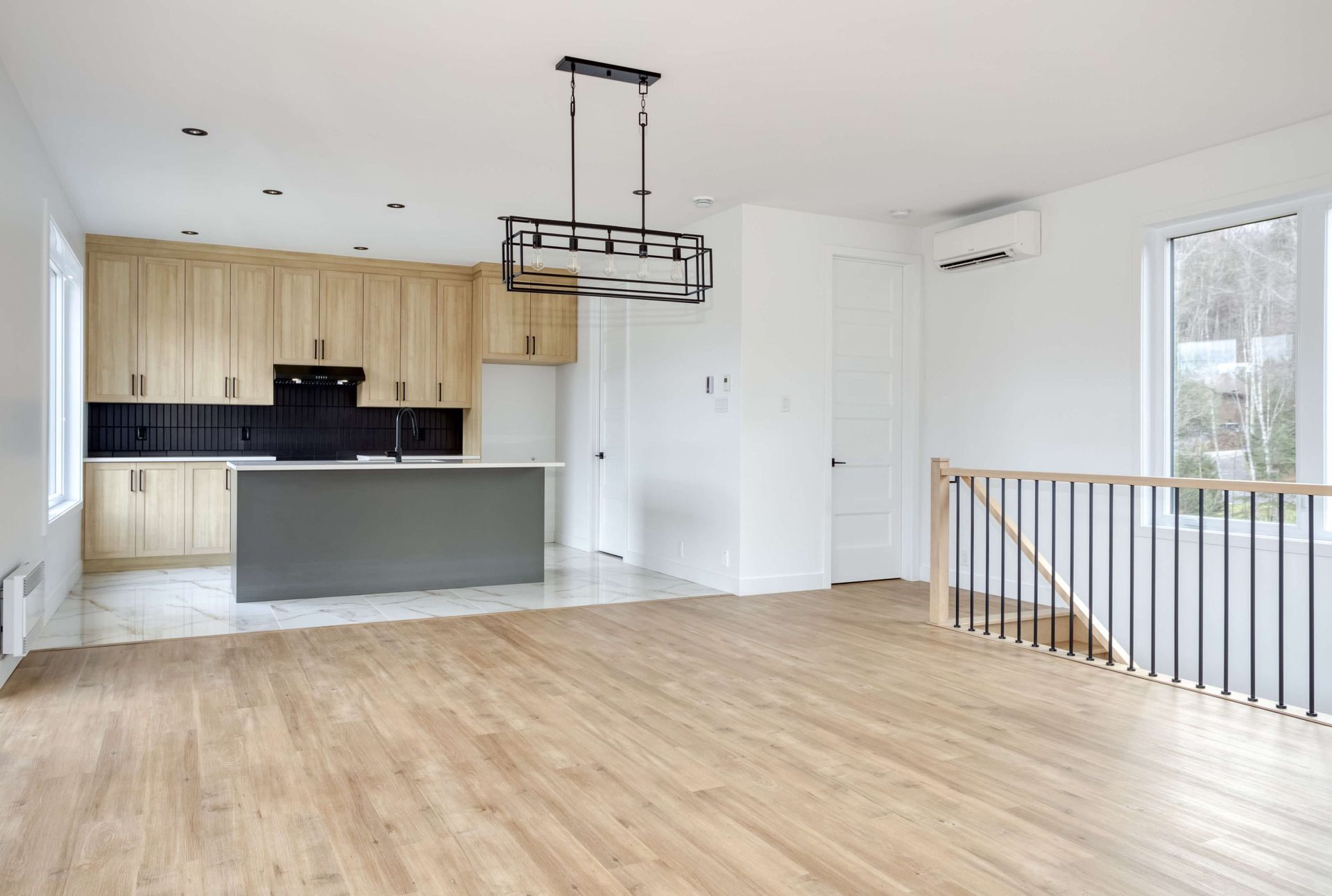 Cuisine moderne avec armoires en bois clair, îlot gris et parquet.