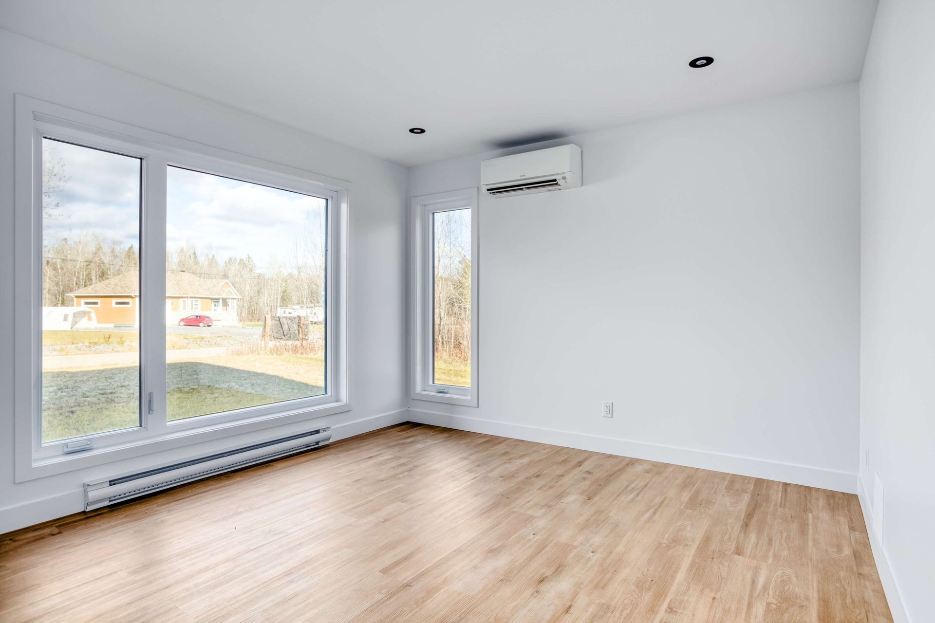 Pièce vide avec de grandes fenêtres, des murs blancs et un sol imitation bois. Climatiseur mural.