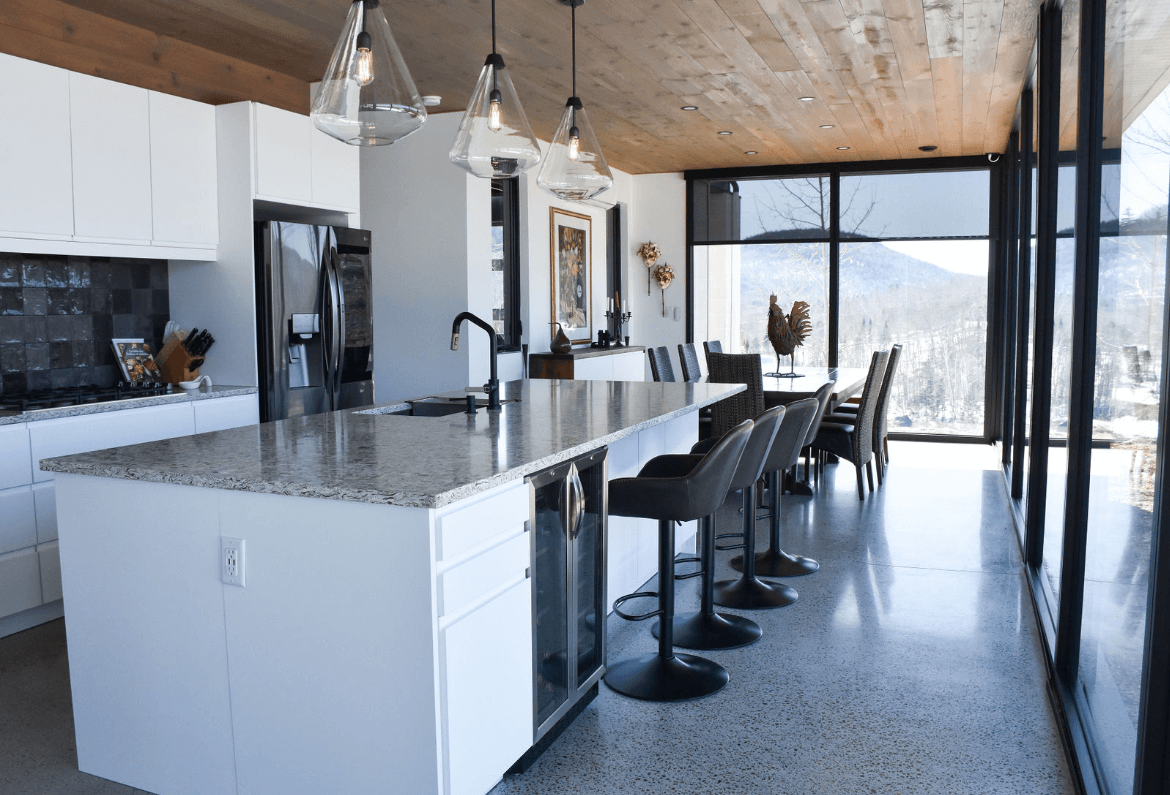 Cuisine moderne avec armoires blanches, îlot central avec comptoir en granit et fenêtres allant du sol au plafond.