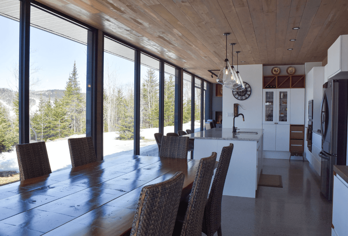 Longue table à manger dans une cuisine moderne avec de grandes fenêtres donnant sur un paysage enneigé.