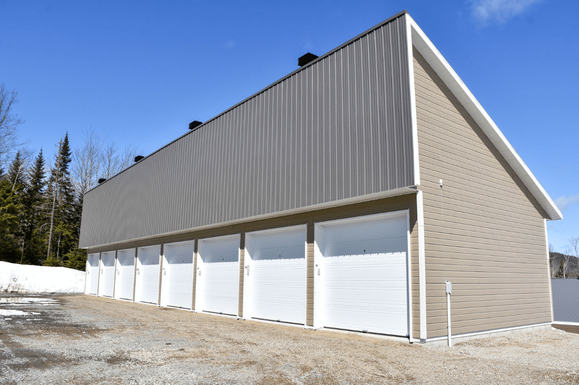 Des box de stockage aux portes blanches, aux murs beiges et au toit en tôle ondulée, sous un ciel bleu.