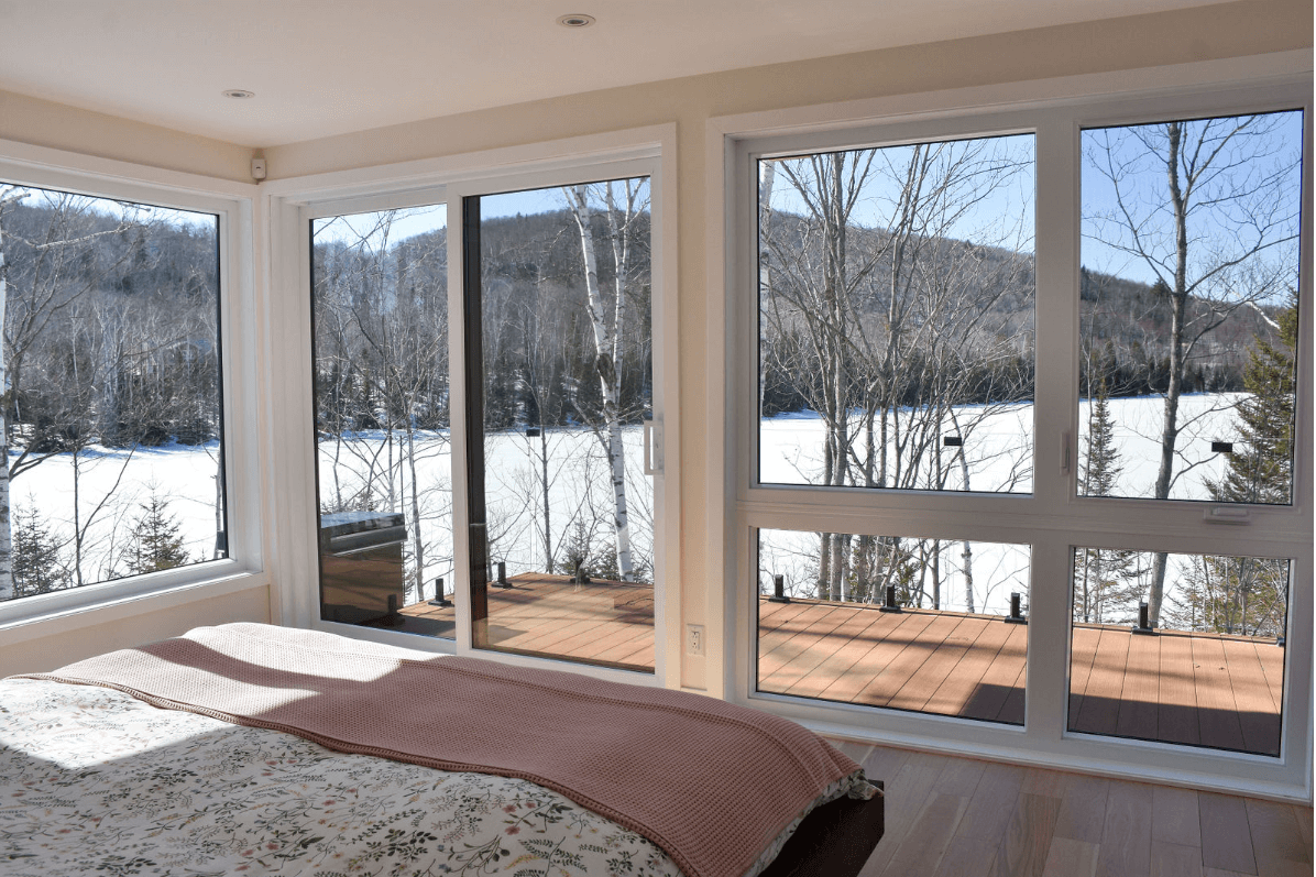Chambre avec de grandes fenêtres donnant sur un paysage enneigé et un lac. Couverture rose sur le lit.
