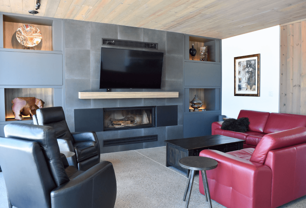 Salon avec cheminée, télévision, canapé rouge, fauteuil inclinable noir et niches murales. Mur en pierre grise.