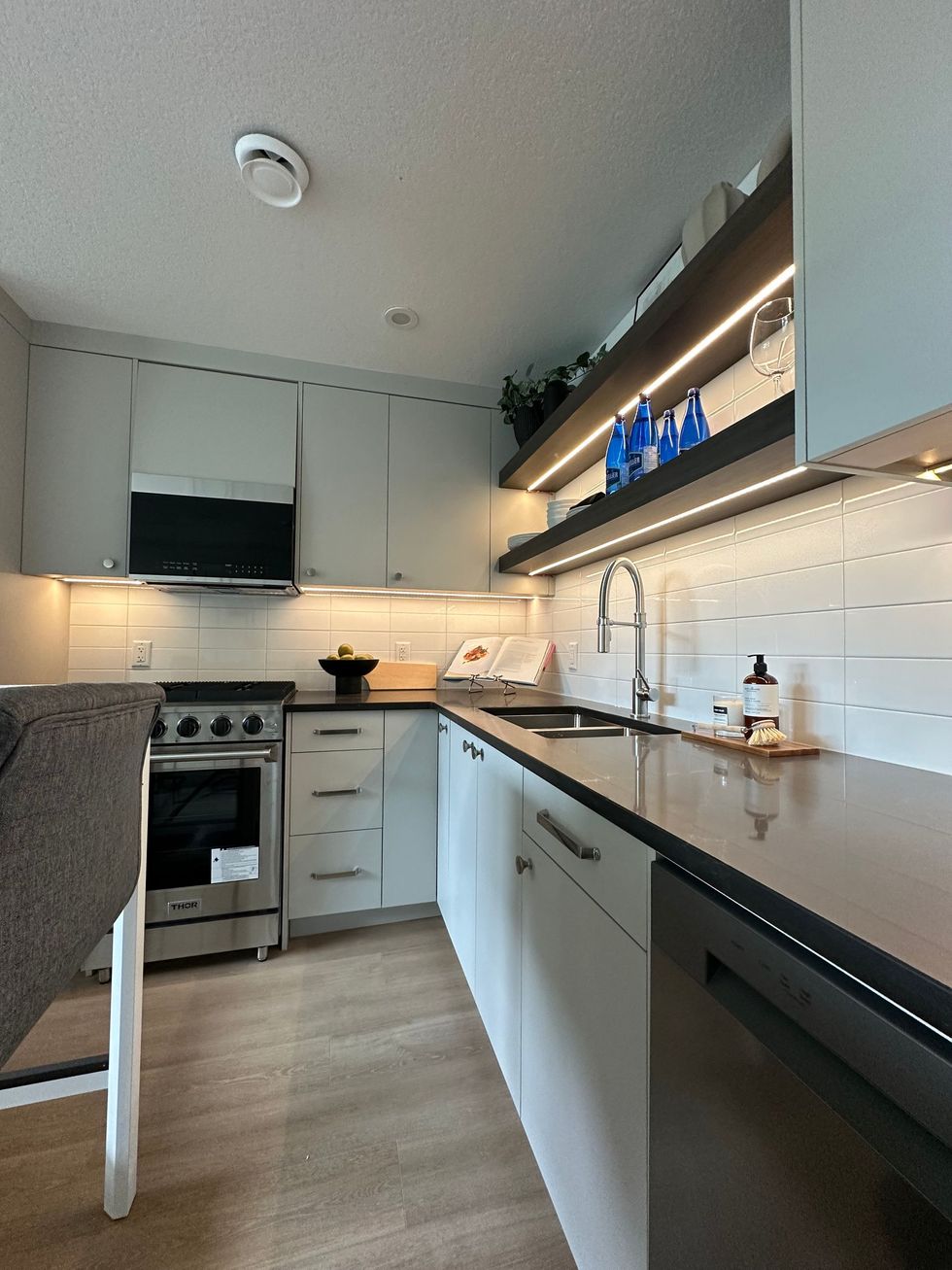 Small, modern kitchen with gray countertops, white cabinets, and stainless steel appliances.