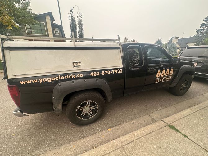 Black truck with white topper parked on a street, advertising 